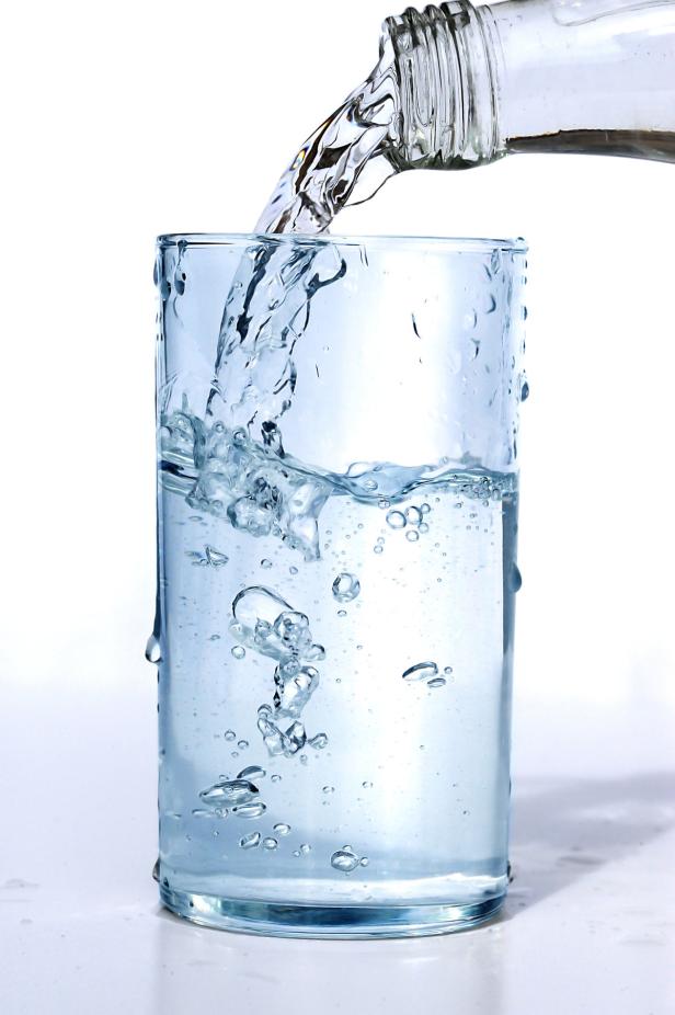 Wasser wird aus einer Glasflasche in ein Glas gegossen.
