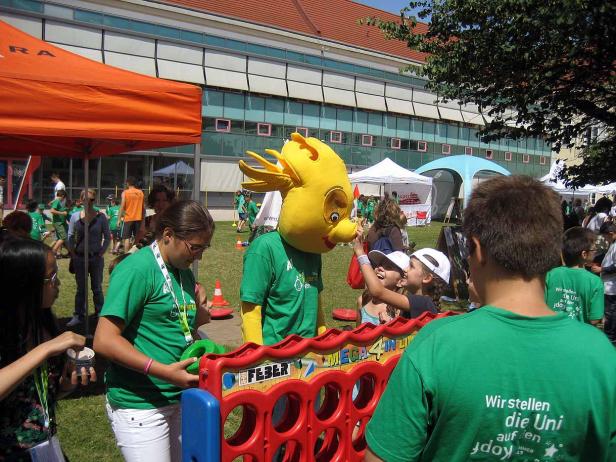 Ein gelbes Maskottchen interagiert mit Kindern auf einer Veranstaltung im Freien.