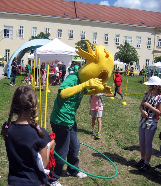 Eine Person im gelben Kostüm hantiert mit einem Hula-Hoop-Reifen auf einer Veranstaltung im Freien.