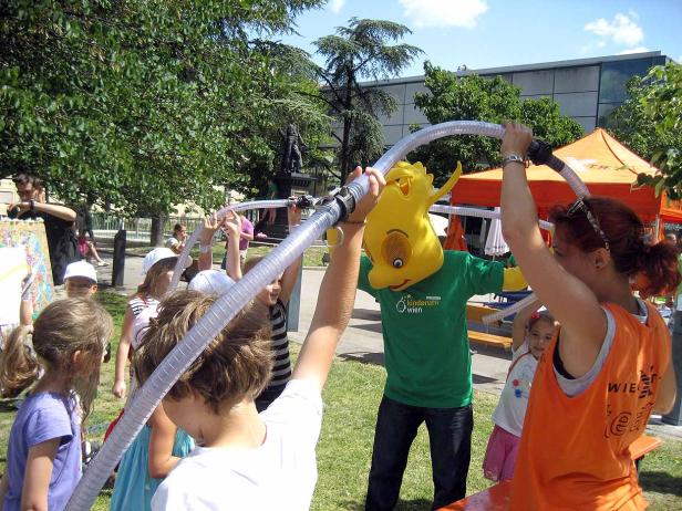 Kinder und ein Maskottchen halten gemeinsam einen Schlauch in die Luft.