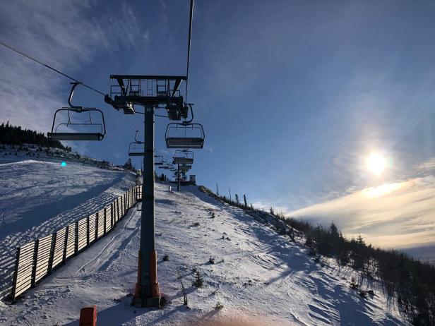 Ein Skilift führt einen verschneiten Hang hinauf, mit blauem Himmel und Sonnenschein.