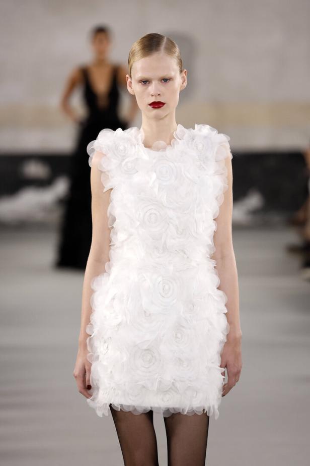 Ein Model präsentiert ein weißes, ärmelloses Minikleid mit floralen Applikationen.
