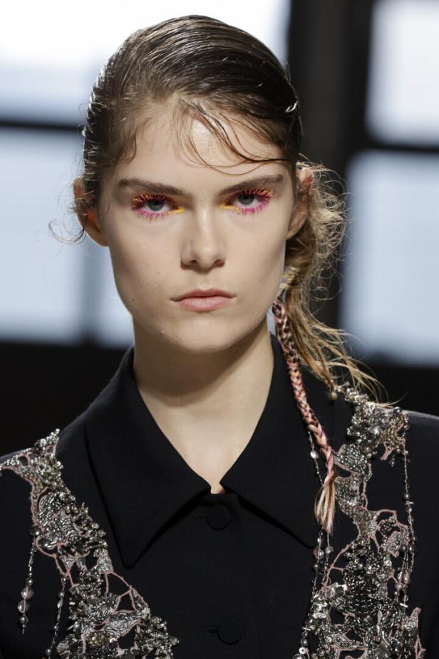 Ein Model mit farbiger Wimperntusche und einem schwarzen, verzierten Oberteil.