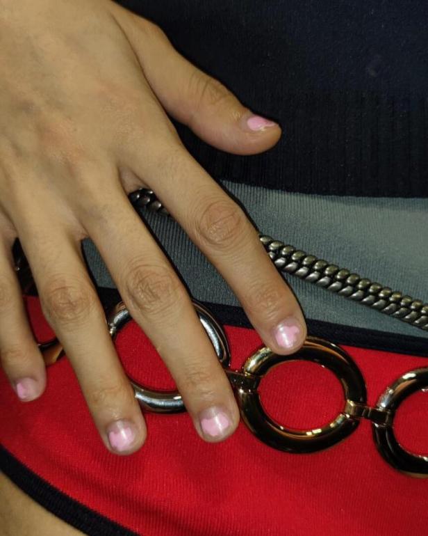Eine Hand mit rosa lackierten Nägeln berührt einen goldenen Kettengürtel.