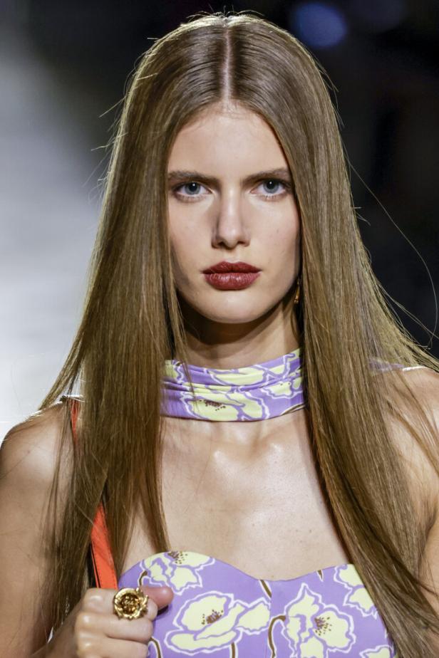 Eine Frau mit langen, glatten Haaren und einem lila-gelben Blumenmuster-Top.