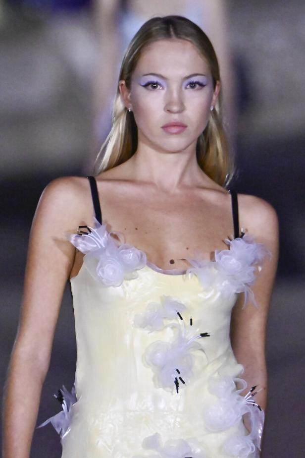 Ein Model mit lila Lidschatten trägt ein gelbes Kleid mit weißen Blumenapplikationen.