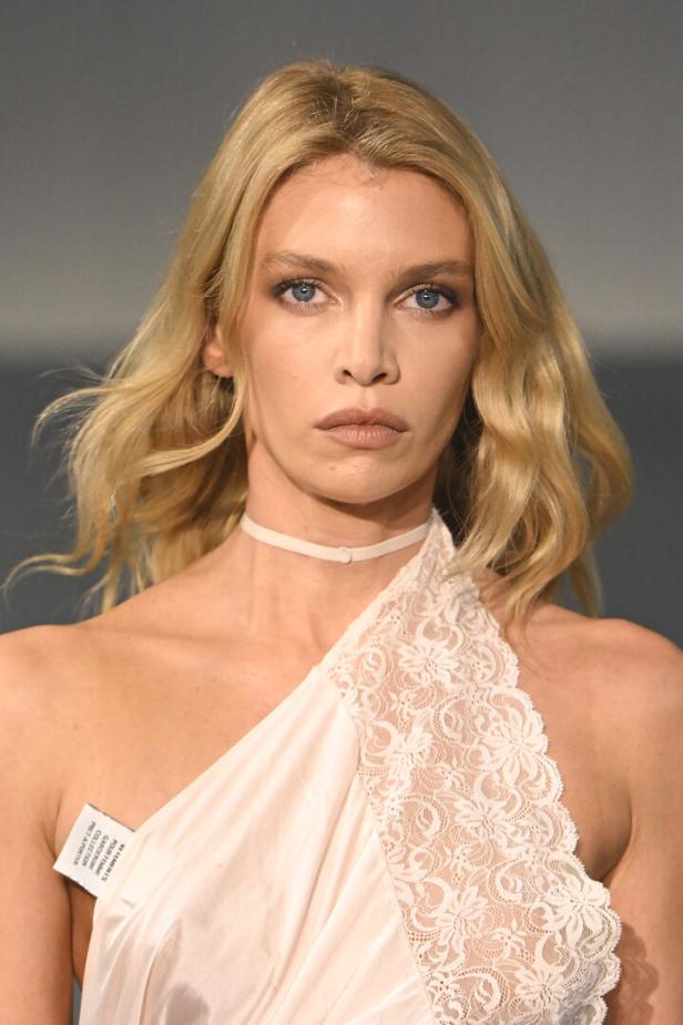 Eine blonde Frau mit blauem Blick trägt ein trägerloses Kleid mit Spitze und ein Halsband.