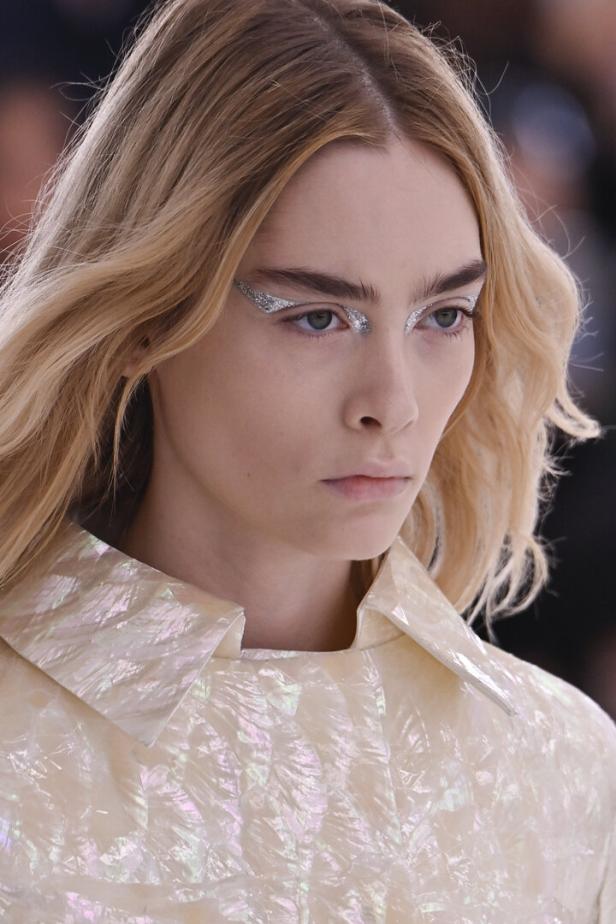 Eine Frau mit blonden Haaren und auffälligem silbernen Glitzer-Make-up um die Augen.