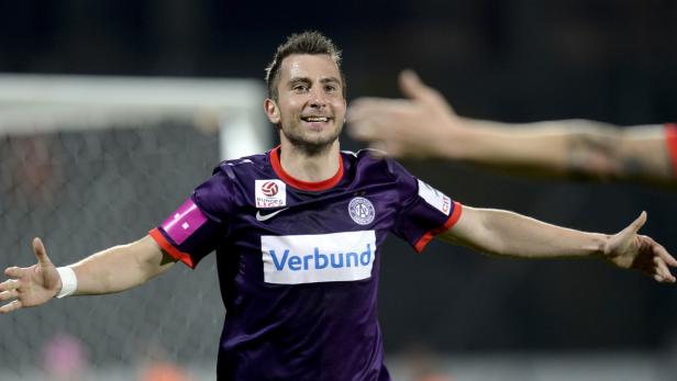 Ein Fußballspieler in lila Trikot jubelt mit ausgestreckten Armen.