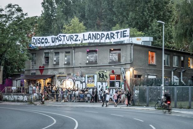 Menschen stehen am Morgen Schlange vor dem About Blank. Das Gebäude ist mir Graffiti und politischen Parolen besprüht. Auf dem Dach prangt ein Transparent mit der Aufschrift: Disco. Umsturz. Landpartie.