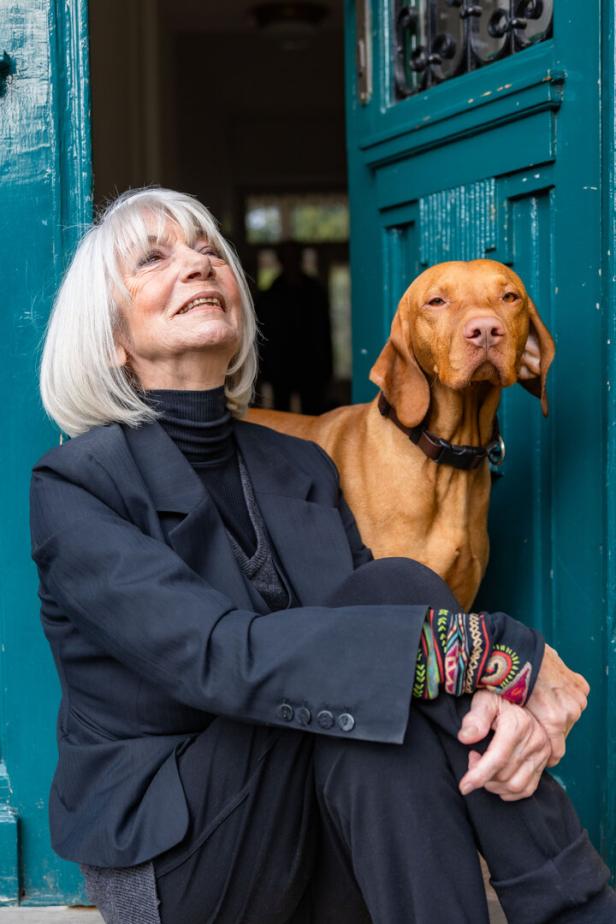 Eine ältere Frau sitzt neben ihrem Magyar Vizsla vor einer blauen Tür.