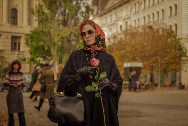 Eine Frau mit Kopftuch und Sonnenbrille hält eine Rose in der Hand.