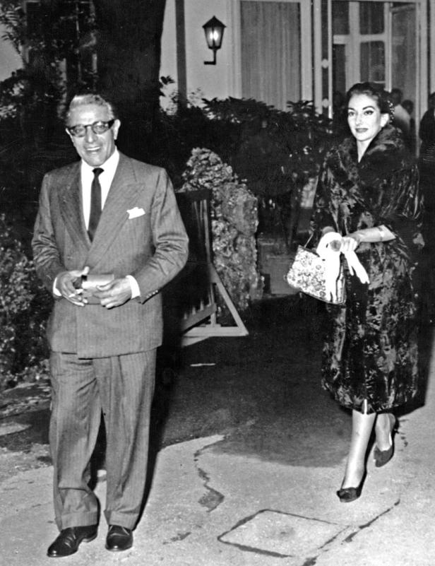 Maria Callas mit einem Mann im Anzug vor einem Gebäude.
