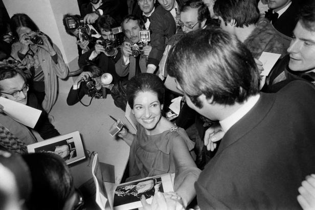 Maria Callas signiert Autogramme, umringt von Fotografen.