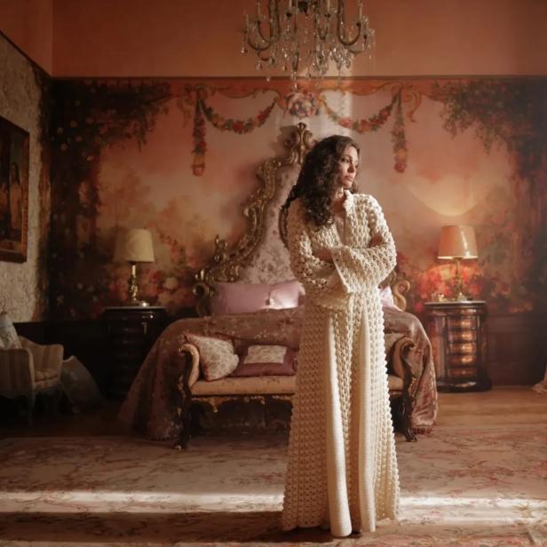 Eine Frau steht in einem opulenten Schlafzimmer mit verschränkten Armen.
