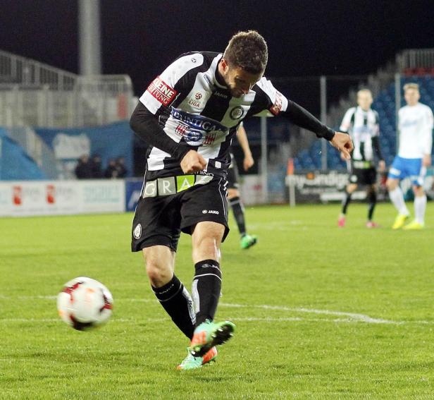 Ein Fußballspieler schießt den Ball auf einem grünen Rasen.