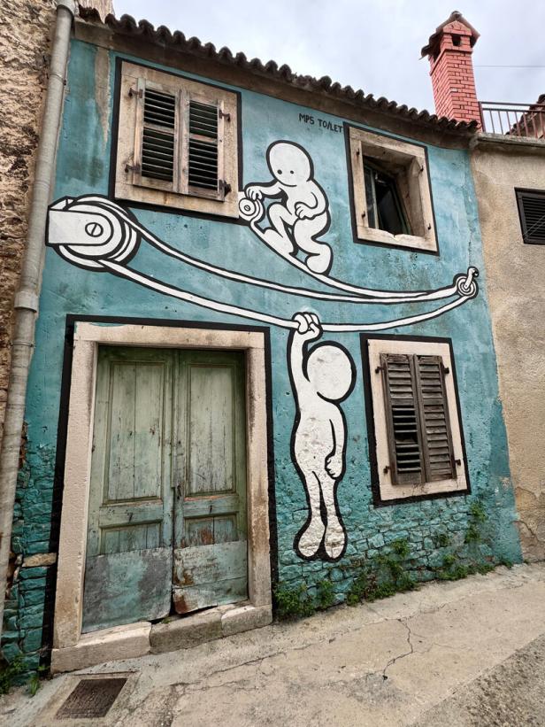 Ein blaues Haus mit einem Graffiti, das zwei Comicfiguren an einem Seil zeigt.