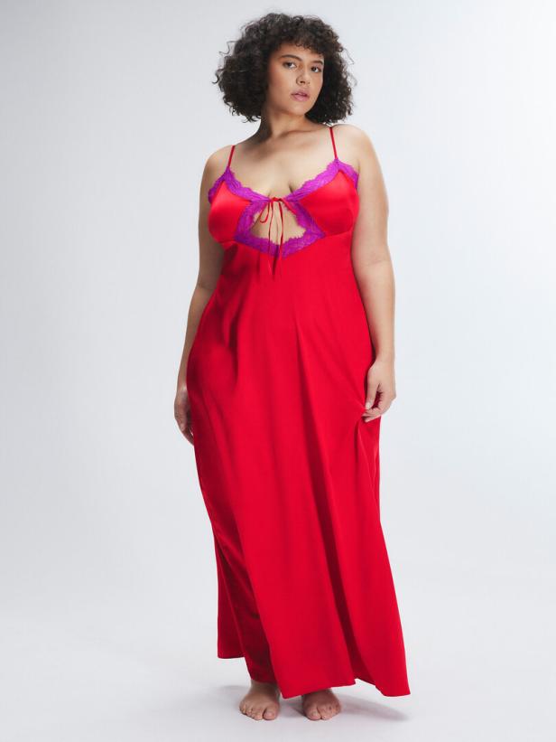Eine Frau mit lockigem Haar trägt ein rotes, bodenlanges Kleid mit lila Spitze.
