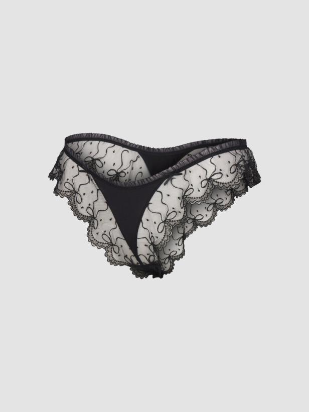 Eine schwarze Damenslip mit Spitze und Schleifenmuster vor einem grauen Hintergrund.