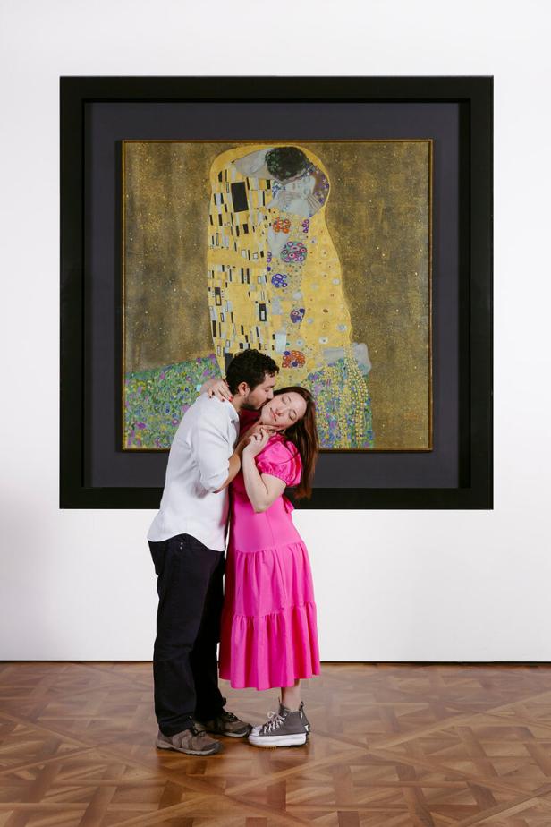 Ein Paar umarmt sich vor Gustav Klimts Gemälde „Der Kuss“.