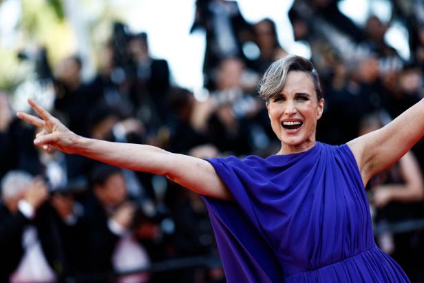 Andie MacDowell auf dem roten Teppich, die ein blaues Kleid trägt und ein Victory-Zeichen macht.