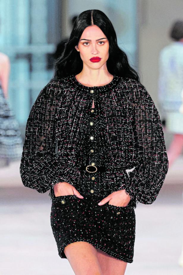 Eine Frau mit roten Lippen trägt ein Tweed-Ensemble mit Puffärmeln.