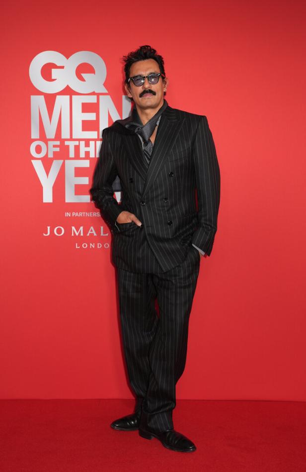 Ein Mann im Anzug posiert vor einem roten Hintergrund bei den „GQ Men of the Year“-Awards.