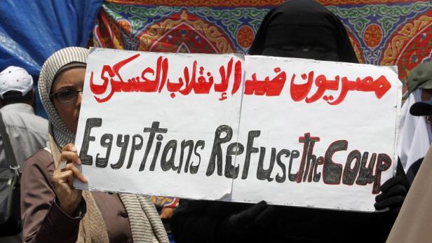 Zwei Frauen halten Schilder mit arabischer und englischer Aufschrift gegen einen Putsch.