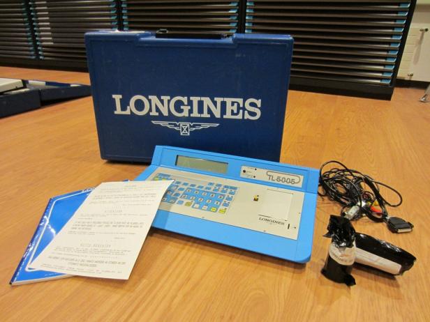 Ein blaues Longines TL-5005 Zeitmessgerät mit Zubehör und Koffer auf einem Holztisch.