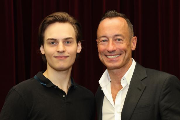 Falco und ein Intendant stehen vor einem roten Vorhang.
