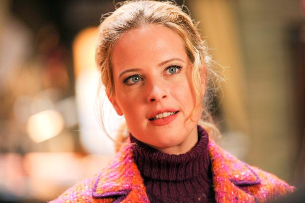 Porträt einer blonden Frau mit blauen Augen in einem bunten Mantel.