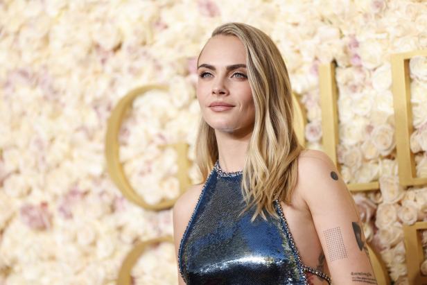 Cara Delevingne posiert vor einer Wand aus Rosen.