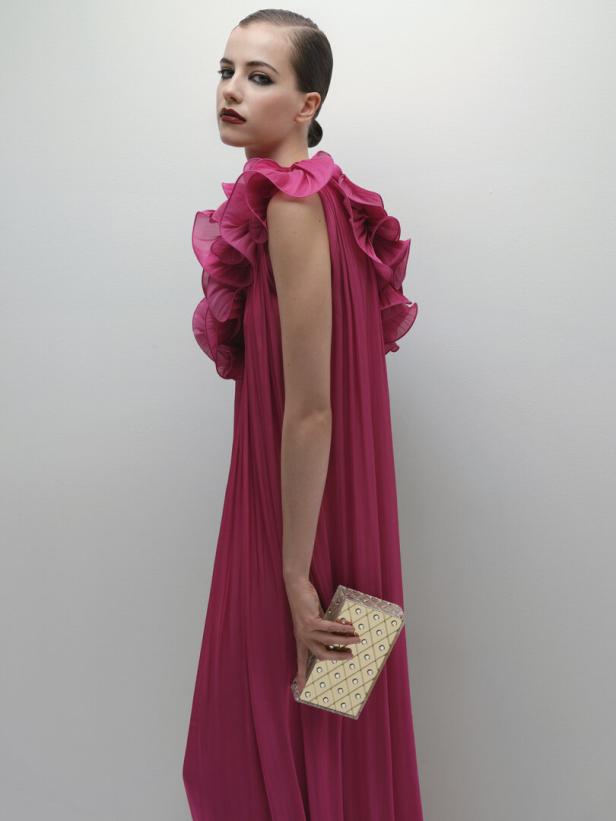 Eine Frau in einem pinkfarbenen Kleid mit Rüschen hält eine goldene Clutch.