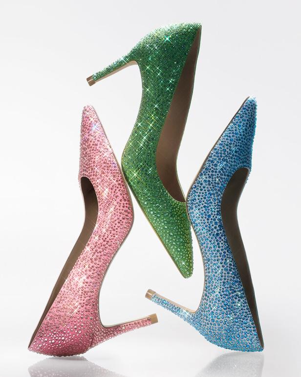 Drei glitzernde High Heels in den Farben Pink, Grün und Blau stehen auf einer weißen Oberfläche.