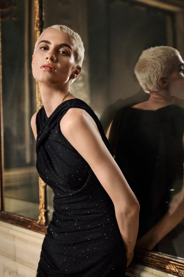 Eine Frau mit kurzem, blondem Haar trägt ein schwarzes, glitzerndes Kleid.