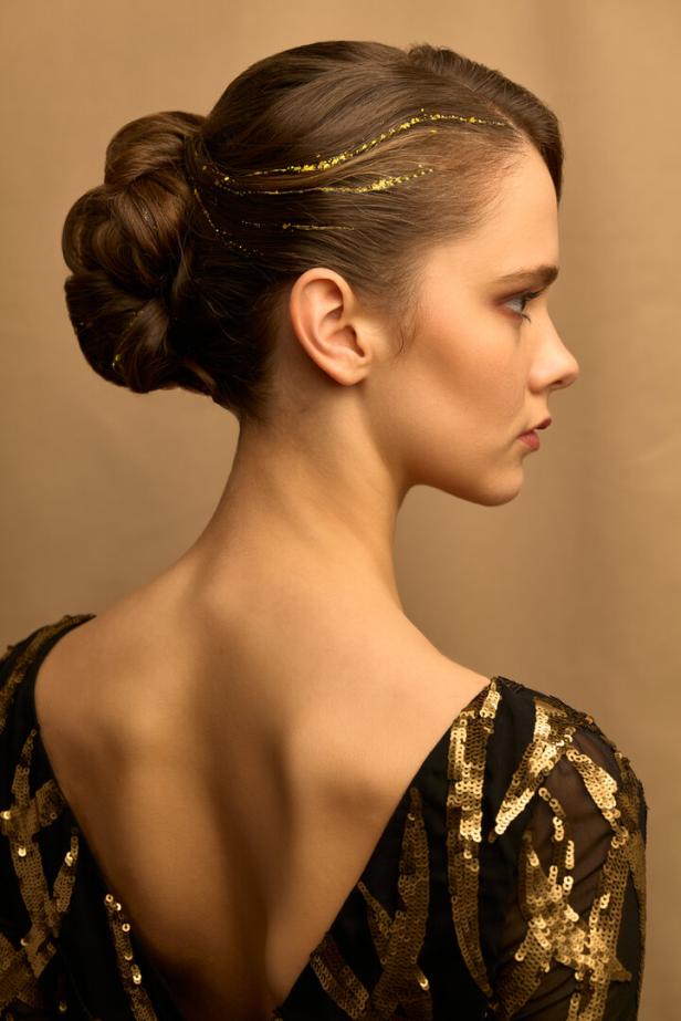 Eine Frau mit Hochsteckfrisur und goldenen Akzenten im Haar trägt ein paillettenbesetztes Kleid.