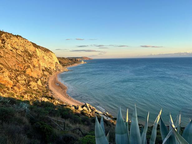 Blick auf einen Sandstrand und das blaue Meer unter einem klaren Himmel.
