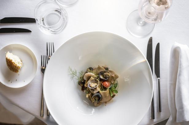 Ein Teller Pasta mit Venusmuscheln und Tomaten auf einem weißen Tisch.