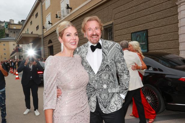 Ein Mann in einem gemusterten Sakko und eine Frau in einem glitzernden Kleid posieren für ein Foto.