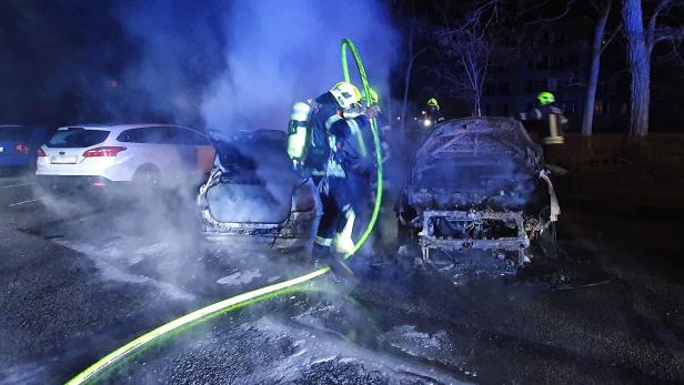 Feuerwehrmänner mit Schlauch löschen zwei Autos 