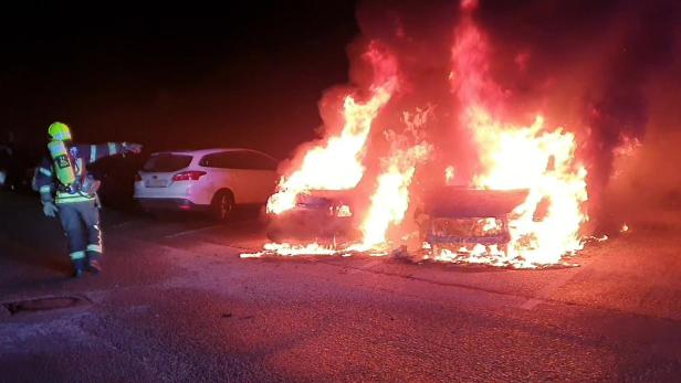 Brennende Fahrzeuge und links von ihnen ein Feuerwehrmann