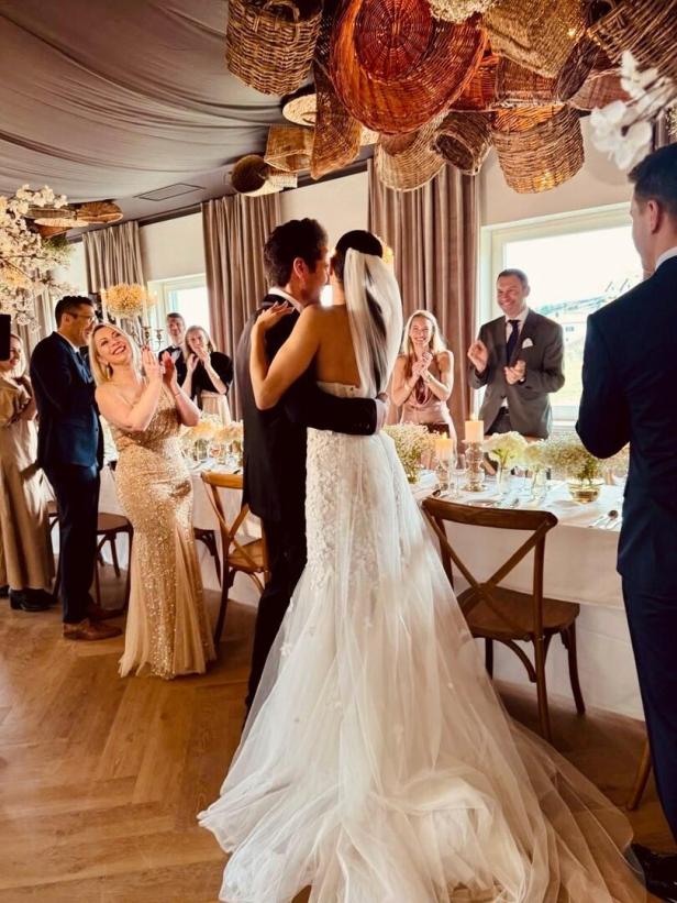 Hochzeitspaar vor einer festlich geschmückten Tafel, Hochzeitsgäste applaudieren ihnen.