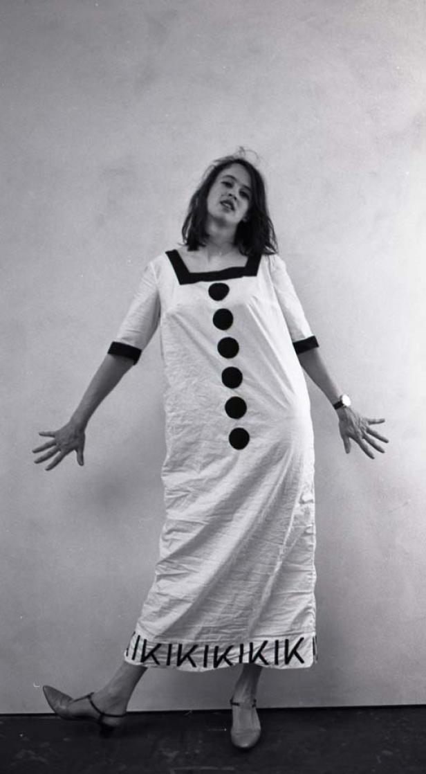 Eine Frau in einem weißen Kleid mit schwarzen Punkten und „KIKI“-Aufschrift am Saum posiert.