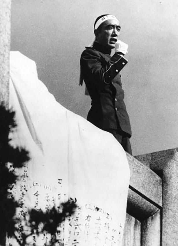 Mit Stirnband und Uniform skandiert Yukio Mishima am Balkon.