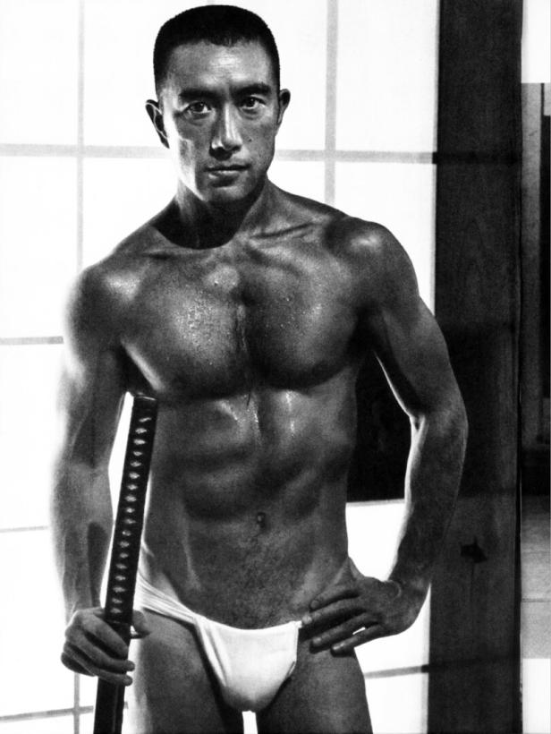 Yukio Mishima nur mit einem Slip gekleidet, muskulös und ein Samuraischwert in der Hand.