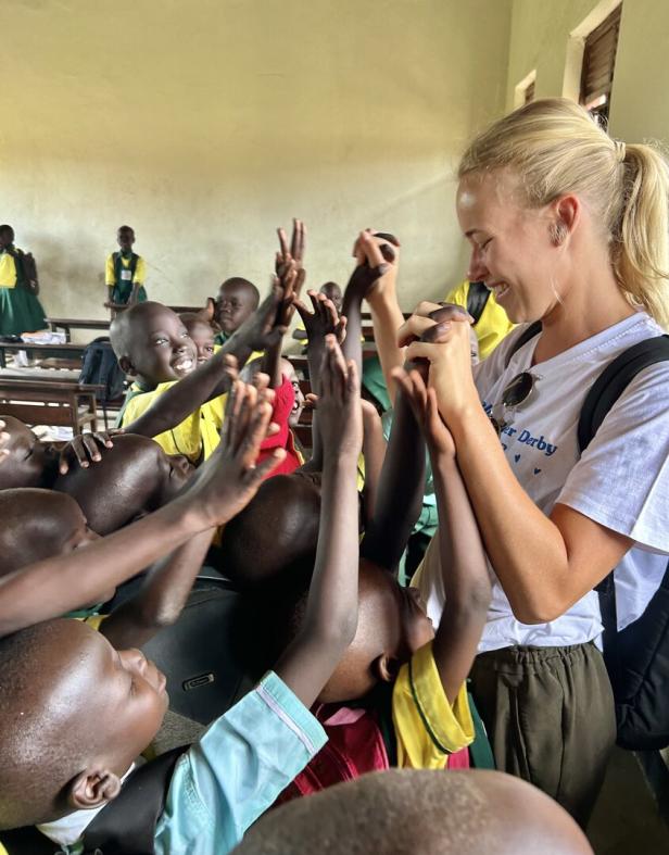 Eine junge Frau gibt einer Gruppe afrikanischer Schulkinder ein High-Five.