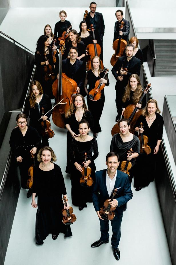Ein Musikensemble steht mit ihren Instrumenten zusammen auf einer Freifläche. Alle tragen schwarz.