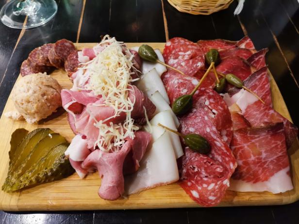 Eine Platte mit Wurst, Schinken, Speck, Griebenwurst, Gewürzgurken und Kapernäpfeln.