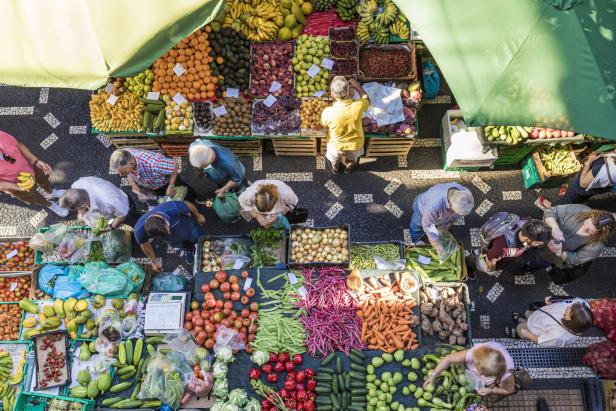 Eine Vogelperspektive auf einen Marktstand mit Obst und Gemüse und mehreren Kunden.