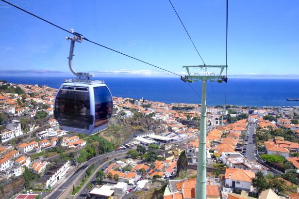 Eine Seilbahn schwebt über eine Stadt mit roten Dächern und Blick auf das Meer.